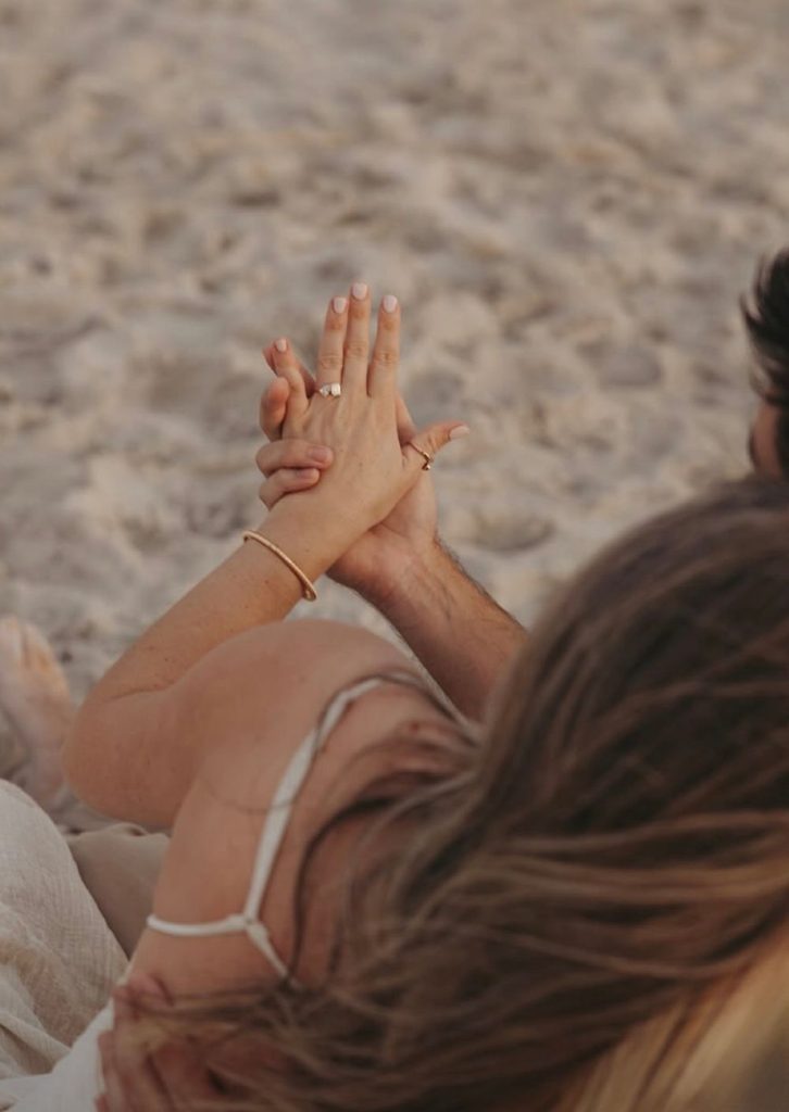 Hands with an engagement ring held up over the sand