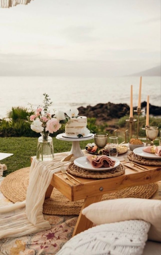 Picnic table with a white cake, pink napkins and candles beside the sea