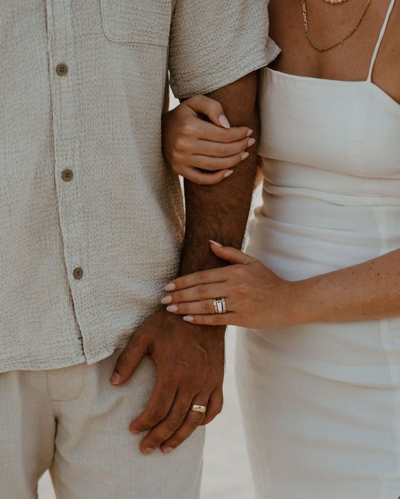 A couple in linen standing arm in arm, wedding rings visible